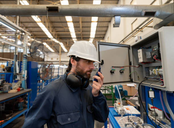 handsome engineer using a walkie-talkie while looking at a switch board of a manufaturing water pump factory - manufaturing imagens e fotografias de stock