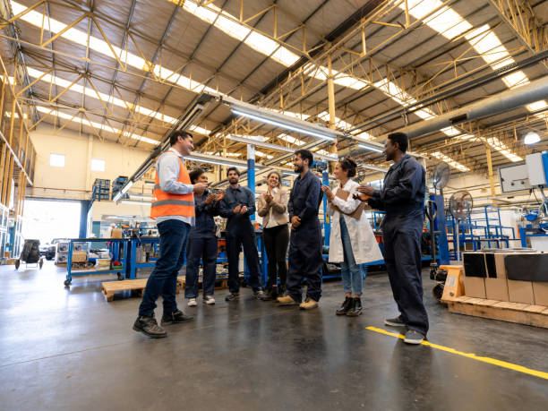 istock Manager at a factory congratulating a blue collar worker and team applauding 1198042384