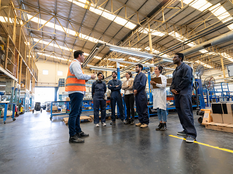 Manager instructing a diverse team of engineers, blue collar workers and quality inspectors at a factory - Manufacturing concepts