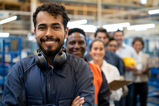 Alegre apuesto trabajador de cuello azul y equipo de ingenieros en una fábrica de pie en una fila sonriendo a la cámara photo