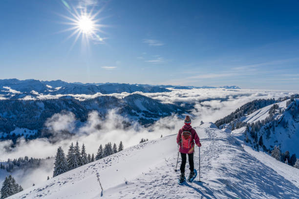 senior woman snowshoeing above a sea of fog nice senior woman snowshoeing on the Nagelfluh chain above a sea of fog over Bregenz Wald mountains, Hochgrat, Steibis,Bavarian alps, Germany allgau stock pictures, royalty-free photos & images