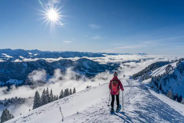 nice senior woman snowshoeing on the Nagelfluh chain above a sea of fog over Bregenz Wald mountains, Hochgrat, Steibis,Bavarian alps, Germany