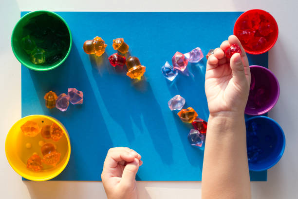istock Child hand separating by color multicolored toy stones scattered on the blue surface into colorful cups 1198047720