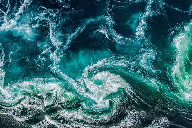 Photo of Abstract background. Waves of water of the river and the sea meet each other during high tide and low tide. Whirlpools of the maelstrom of Saltstraumen, Nordland, Norway