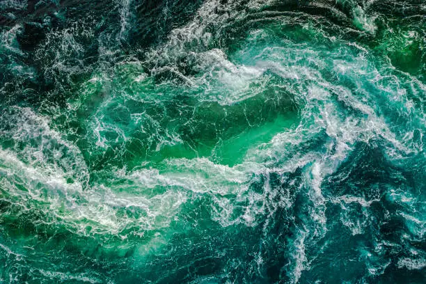 Photo of Abstract background. Waves of water of the river and the sea meet each other during high tide and low tide. Whirlpools of the maelstrom of Saltstraumen, Nordland, Norway