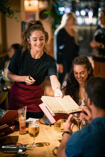 A waitress giving a menu to a customer, who is dining at a restaurant in Newcastle-Upon-Tyne.