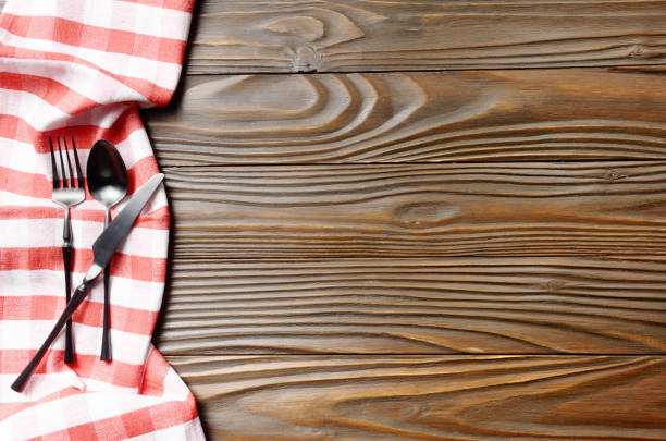 istock Red checkered napkin and silverware on brown wooden kitchen table with copy-space. Top view 1198054566