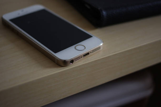 used gold iphone 5 with white panel and thunderbolt interface on light yellow wooden table - iphone iphone5 iphone 5 telephone imagens e fotografias de stock