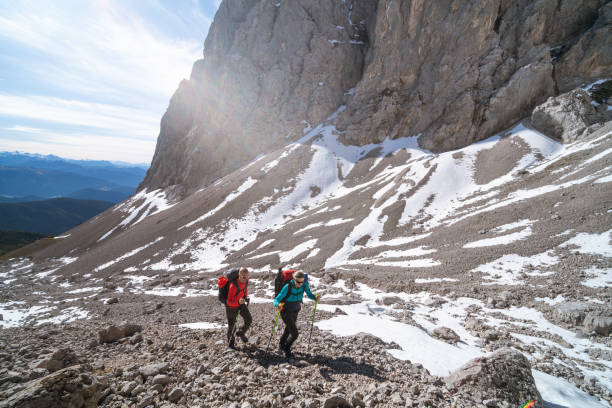 mature adult hiking mountaineer couple on challenging asscent over boulder, scree, stones, rocks and some snow high up in alpine mountain landscape on sunny autumn day