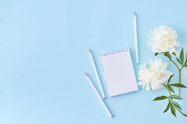 istock Flat lay blogger or freelancer workspace with a notebook and white peonies on a blue background 1198063891
