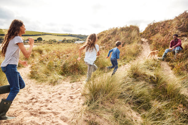 istock Three Children Having Fun Exploring In Sand Dunes On Winter Beach Vacation Run To Father 1198066144