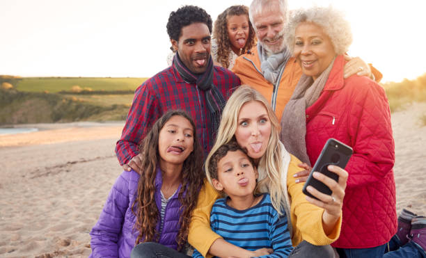 istock Multi-Generation Family Sitting By Fire On Winter Beach Vacation Taking Selfie 1198068527