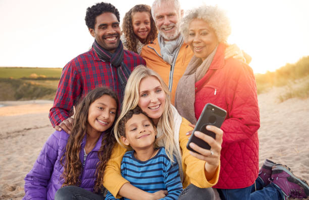 istock Multi-Generation Family Sitting By Fire On Winter Beach Vacation Taking Selfie 1198069633