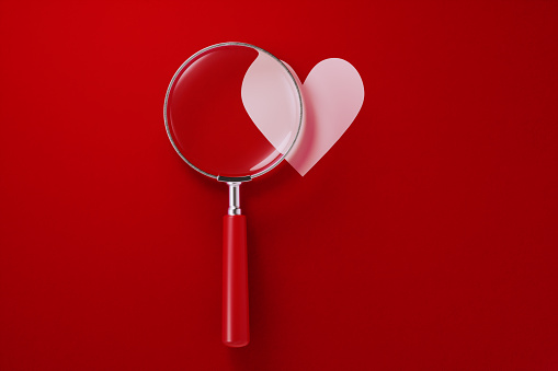 Magnifier and heart shape over red background. Horizontal composition with copy space.