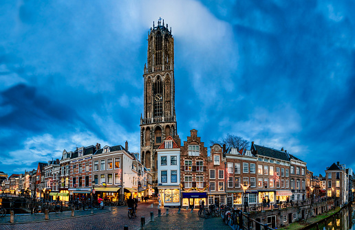Utrecht, the Netherlands - December 31st 2013 : Now under multi year construction this multi image panorama shows the famous Utrecht cathedral in early evening winter light on the last day of 2013. Shops in yellow light, people walking and the Dom tower (domtoren) rising against blue evening sky.