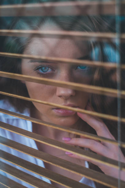 istock Girl looks through blinds 1198075724