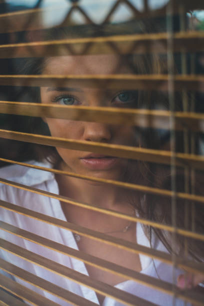 istock Girl looks through blinds 1198075810