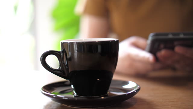 Coffee cup at cafe with woman using mobile phone