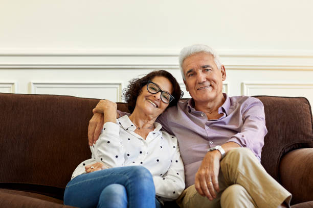 istock Elderly man sitting with arm around woman on sofa 1198077047