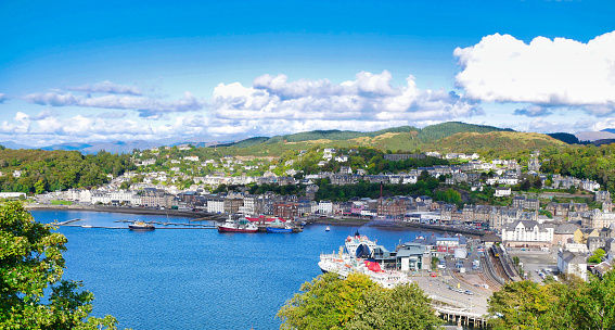 A panoramic view of Oban on the west coast of Scotland, showing the town, ferry terminals and hills in  the background, taken on a sunny day in early autumn