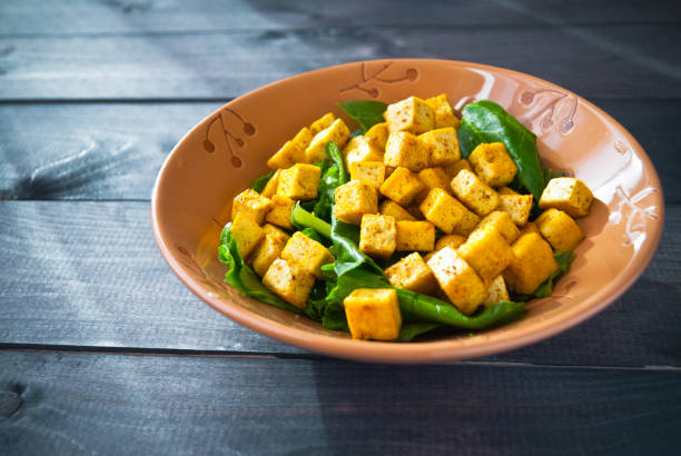 Salad from fried tofu with curry and green leaves of fresh spinach in ceramic bowl. Space for text