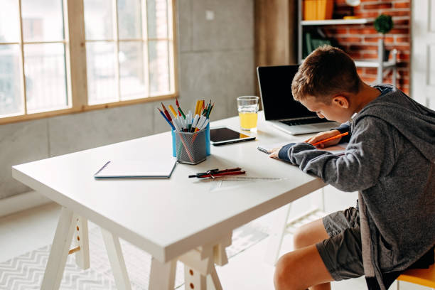 istock Young boy at home writing in school text book at the dining table 1198080797