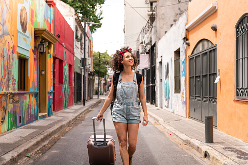 A young woman traveling through Buenos Aires with a backpack and wheeled luggage.