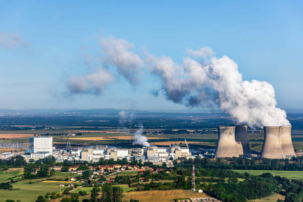 French nuclear power station aerial view in countryside landscape in summer with smoking cooling towers on blue sky Photography of french nuclear power station with four steaming cooling towers smoking on blue sky in summer, in Ain department countryside plain with water condensation. Image taken from high angle view, aerial view, in Bugey, in Ain on the border of Isere department, Auvergne-Rhone-Alpes region in France (Europe). The nuclear power station is located in the middle of a plain landscape in France, near Lyon city. Shot in sunny day summer season with green meadows near small villages. nuclear power station stock pictures, royalty-free photos & images