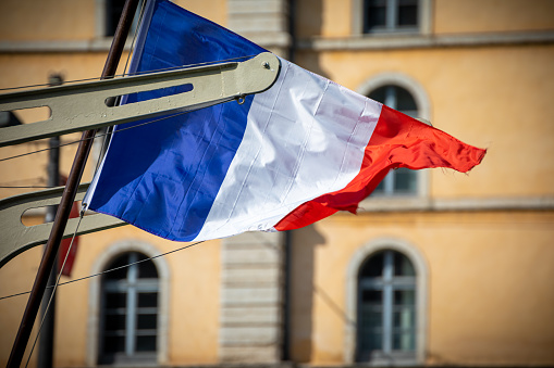 Close-up view in selective focus of the French blue white and red color national flag blowing in the wind on a sunny day on a boat on Saone river in Lyon city in France, Auvergne-Rhone-Alpes region (Europe).