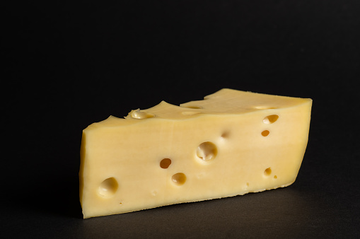 Piece of Maasdam cheese. Triangular piece of Maasdam cheese with large holes on black background