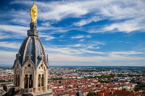 Beautiful Saint Thomas chapel aerial view with golden Virgin Mary statue on top of the steeple seen from the roofs of Basilica Notre Dame de Fourviere built between 1872 and 1884, in a dominant position overlooking the city of Lyon, and dedicated to the Virgin Mary. This image was taken during a sunny summer day in famous Lyon city in Rhone department, Auvergne-Rhone-Alpes region in France (Europe), outside Basilica Notre Dame de Fourviere, on Fourviere hill.