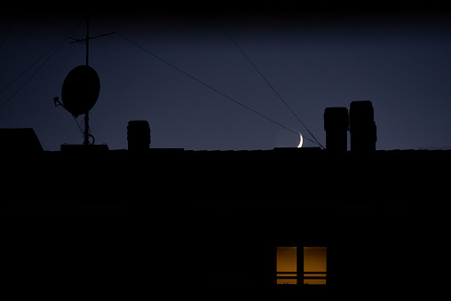 waning moon on roofs with illuminated window