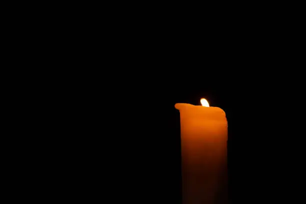 a single orange burning candle in the dark