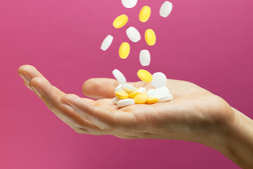 White and yellow medications are pouring dow into a female hand on pink background.