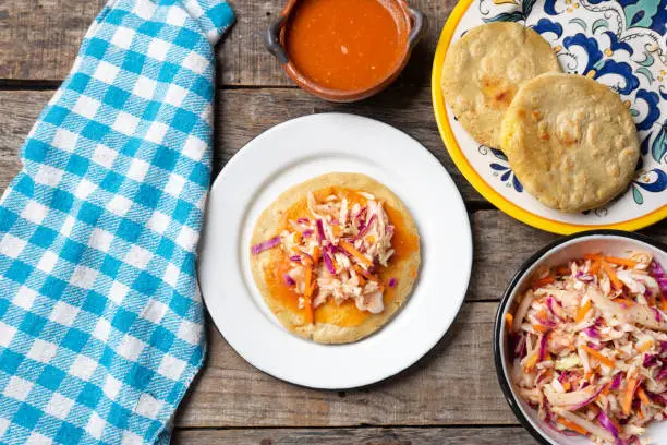 Traditional salvadoran pupusas with coleslaw and tomato sauce on wooden background