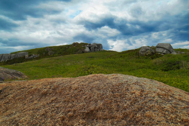 Large rock in the foreground framing a lawn on Sambaqui Hill under a clouded sky.