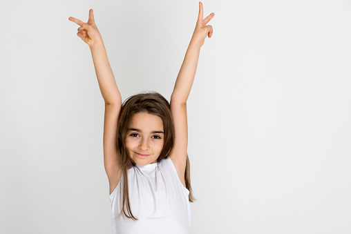 Young smiling girl wearing white t-shirt holding hands up with two fingers looking at camera