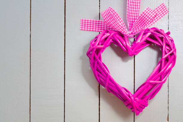 Pink heart hanging from pink ribbon on rose background. Horizontal composition with copy space. Valentine's Day concept.