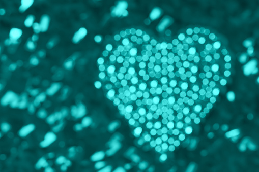 Heart made of turquoise defocused lights on a glittering background. Beautiful bokeh, space for copy.