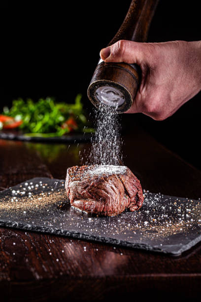 cocina americana. chef sazonar la sal en un jugoso filete de ternera en un restaurante. imagen de fondo, espacio de copia - sal condimento fotografías e imágenes de stock