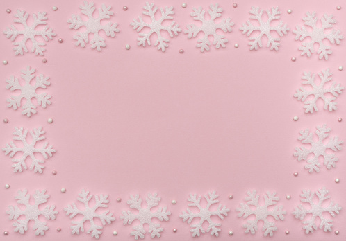 Christmas pink background with white snowflakes and beads. New Year greeting card. Flat lay style.