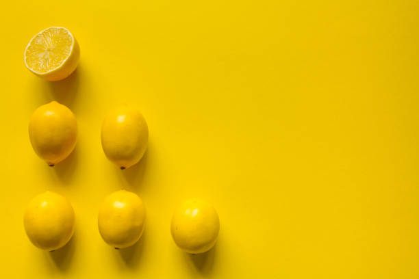 Top view whole and sliced ripe lemon laid out in several rows on a yellow surface, concept of health and vitamins
