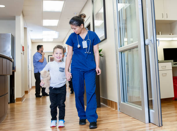 istock Elementary age boy patient holding teddy bear and holding nurses hand in hospital 1198122976