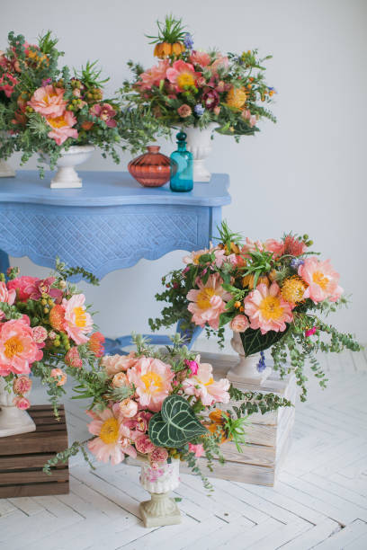 istock Workshop on creating a bouquet and floral arrangements in style of boho chic. Pink peonies, red roses, green eucalyptus. Bouquets in ceramic vases on wooden coasters and a table. On white background. 1198123796