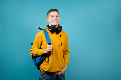 guy with headphones in a yellow sweatshirt on a blue background with a backpack on his shoulder
