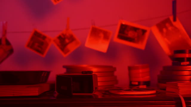 Old developed photos hanging on rope in red dark room of private photo laboratory. Black and white photos print, favorite hobby, renewal of memory records from childhood. Photo development process