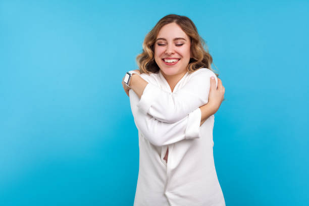 self-esteem, love. portrait of egoistic beautiful woman embracing herself. isolated on blue background - urgency body care young adult people imagens e fotografias de stock