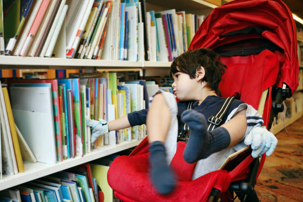 도서관에서 책을 선택하는 빨간 유모차에 장애인 어린 소년 스톡 사진