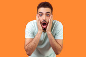 Unbelievable shocking news! Portrait of stunned brunette man keeping mouth wide open in amazement. isolated on orange background