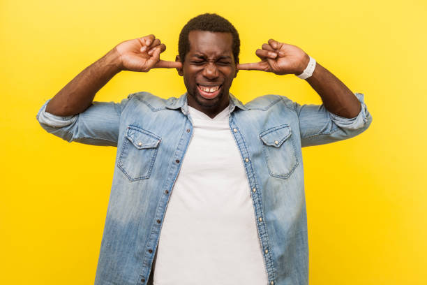 Don't want to hear. Portrait of frustrated irritated man covering ears with annoyed expression, . isolated on yellow background Don't want to hear. Portrait of frustrated irritated man in denim casual shirt covering ears with annoyed expression, ignoring conflict or pressure. indoor studio shot isolated on yellow background man closing ears photos stock pictures, royalty-free photos & images